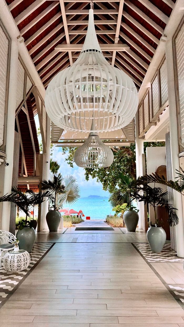 Home Elegant resort entrance with chandeliers leading to a pristine beach view.