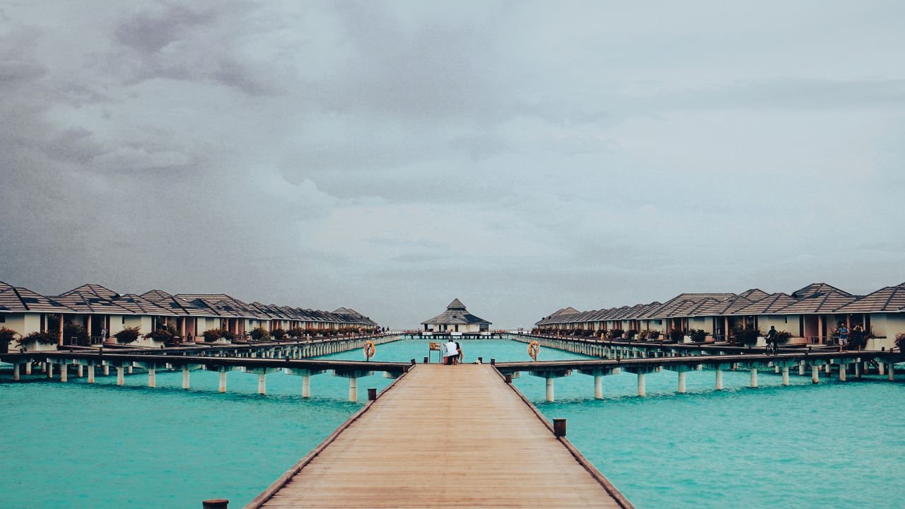 Scenic view of wooden pathway leading to overwater villas in Maldives on a cloudy day.